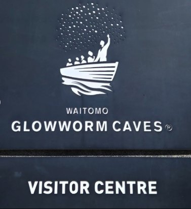 The Waitomo Glowworm Caves visitor centre sign, its logo a boat of passengers under a scatter of glowworms